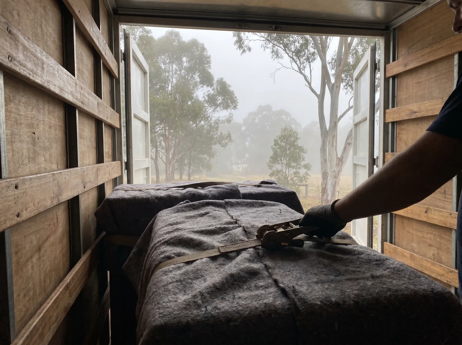 Furniture wrapped in grey moving blankets and strapped to the wall rails inside a removals truck